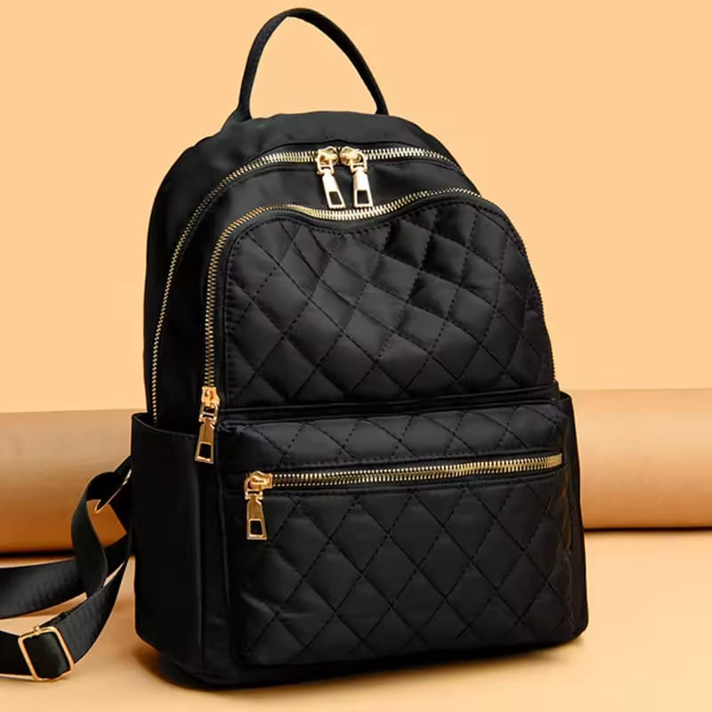 Black quilted backpack with gold zippers on a beige background