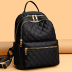 Black quilted backpack with gold zippers on a beige background