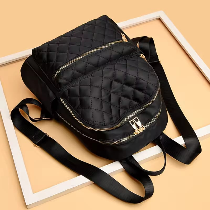 Black quilted backpack with gold zippers on a beige background