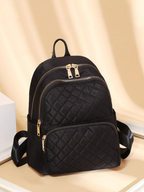Black quilted backpack with gold zippers on a beige background