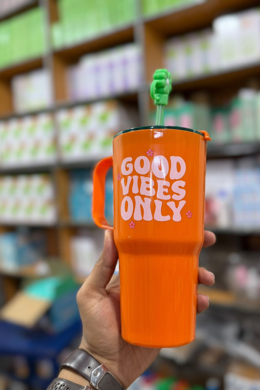 Orange mug with 'Good Vibes Only' text held in a hand, blurred store shelves in the background