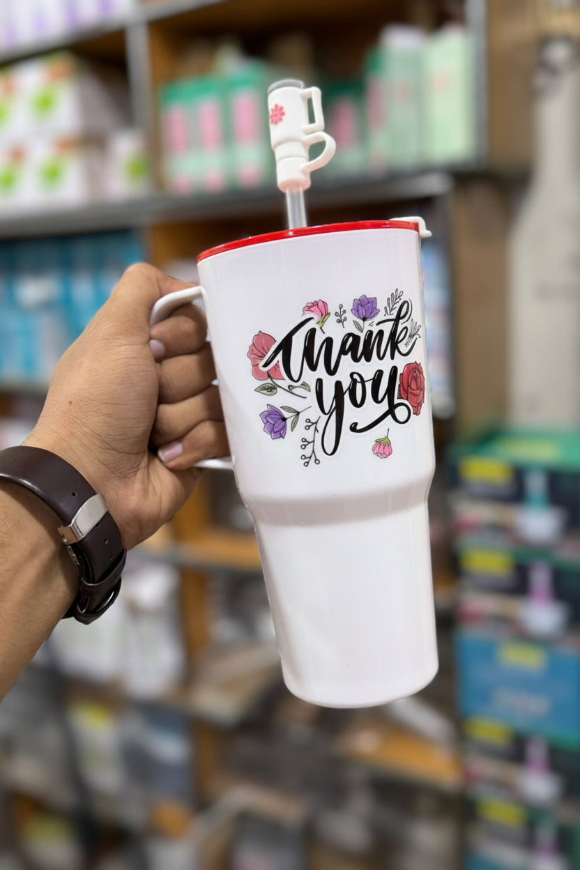 White tumbler with 'Thank you' text and floral designs held by a hand in a store setting.