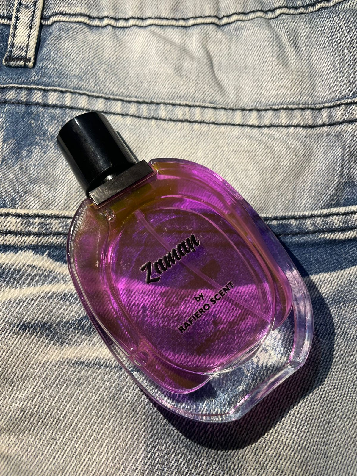 Purple perfume bottle labeled 'Zaman' on a denim background